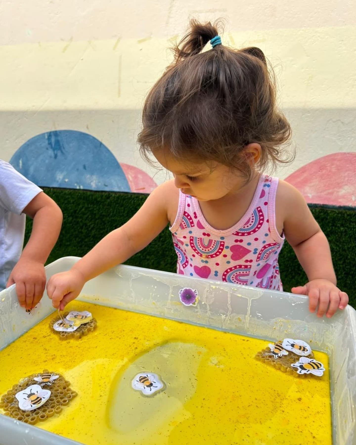 Menina mexendo numa bacia com água amarela e flores de papel