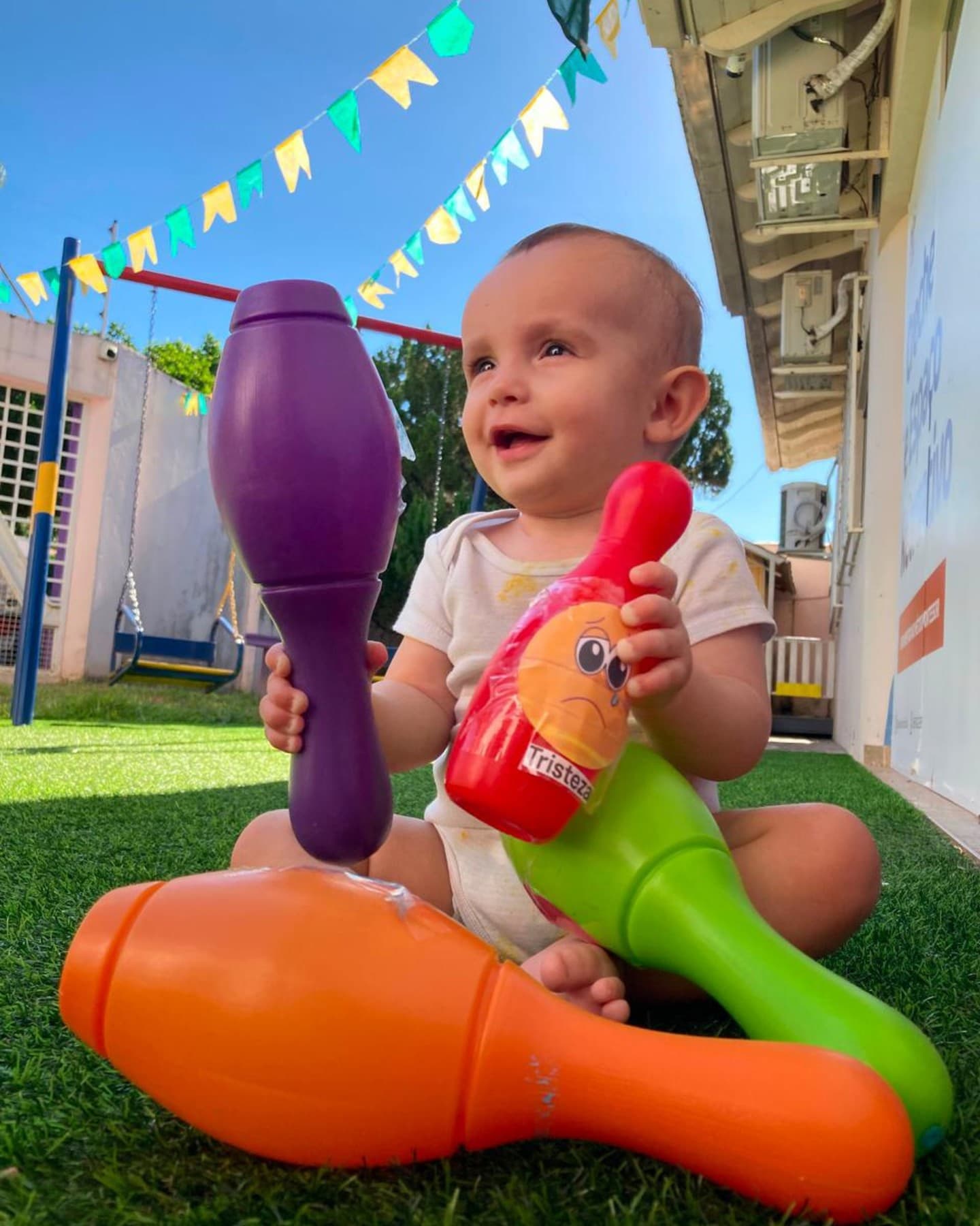 Bebê sentado na grama segurando pinos coloridos de boliche